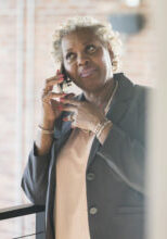 A mature African-American woman in her 50s talking on a mobile phone. She is a businesswoman in an office building.